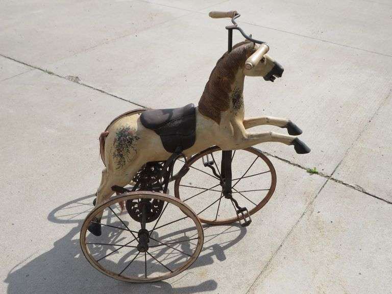 Antique wooden horse tricycle with a cast iron frame, hand-painted details, leather saddle, and wood