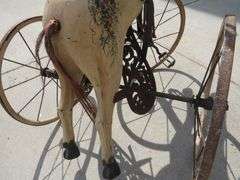 Antique wooden horse tricycle with a cast iron frame, hand-painted details, leather saddle, and wood