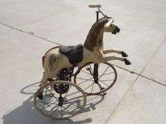 Antique wooden horse tricycle with a cast iron frame, hand-painted details, leather saddle, and wood