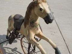 Antique wooden horse tricycle with a cast iron frame, hand-painted details, leather saddle, and wood