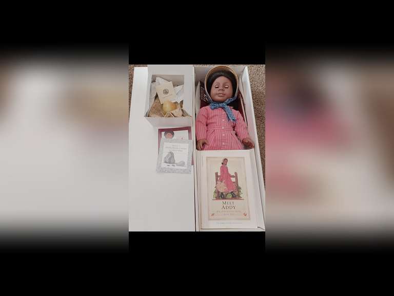 Addy Walker. Addy is one of the first-four original American Girl Dolls. She stands 18 inches tall and wears her original period clothing. She represents life during the midst of the Civil War. She was born into slavery in North Carolina. Addy has been maintained exclusively for display behind glass in a smoke-free environment and she has not been used for play.
Addie comes complete with her accessories, including her book, “Meet Addy”, in the original box. Her WATER GOURD and doll stand packed in separate boxes.