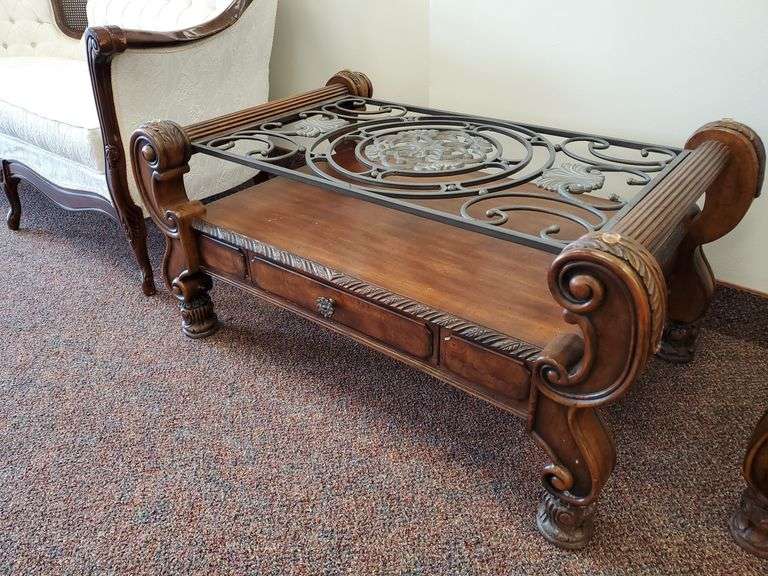 Solid wood coffee table featuring decorative bent metal top, single center drawer, scrollwork and carved accents measuring 40 in W x 26-in D X 20 in H. Missing glass top