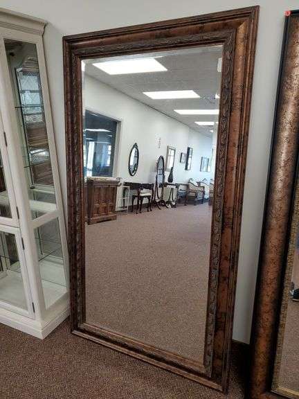 Large bevel edged wall mirror measures 70 in H X 40 in W and features ornate leaf pattern in antique bronze like finish.