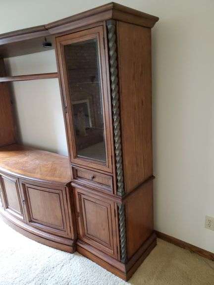 Beautiful solid wood entertainment center featuring beveled edged glass on doors, twisted metal accents in antique bronze finish, glass shelves with overhead lights, and plenty of storage, measures 108 in wide 24 in D X 74 in h. Breaks down into approximately five pieces. Family room.
