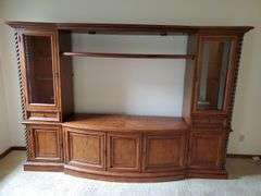 Beautiful solid wood entertainment center featuring beveled edged glass on doors, twisted metal accents in antique bronze finish, glass shelves with overhead lights, and plenty of storage, measures 108 in wide 24 in D X 74 in h. Breaks down into approximately five pieces. Family room.