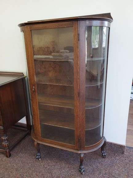 Vintage Solid oak, curved glass Curio cabinet with paw feet and casters features (4) shelves with plate rails. (small repair on door). Measures 36 in W X 14 in D X 62 in H.