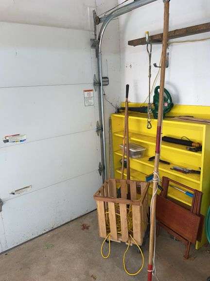 Contents of corner of garage. Featuring rolling basket. Extension cord. Electric blower. Rake and snow shovel. Branch trimmer tool. And miscellaneous other items.