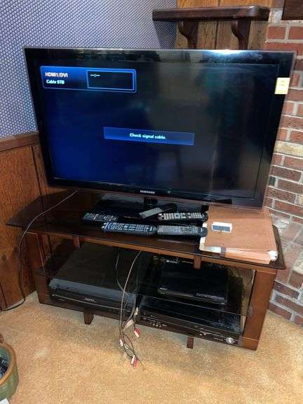 Den. Samsung 40 inch TV model LN40D630M3F. With Sony Blu-ray. Panasonic DVD and VHS. And a Magnavox five disc CD changer. On stand. Remotes included. TV powered on.