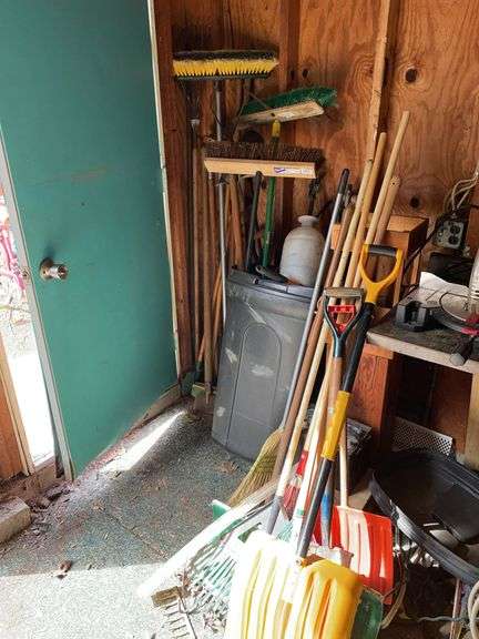 Corner of garage. Large lot of hand tools : rakes, shovel, trash, cans, etc. with trashcan