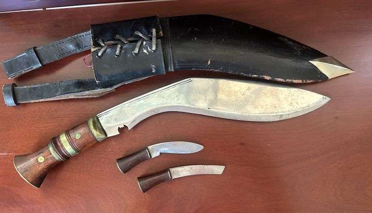 Traditional Kukri knife. Nepal & Australia, from the period of the first world war. With a slightly curved, sharp blade. The black leather sheath is equipped with two small blades.