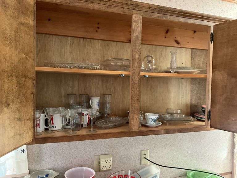 Contents of cupboard: measuring cups, glass bakeware, plastic dinnerware, mugs, cups and saucers, glassware, misc