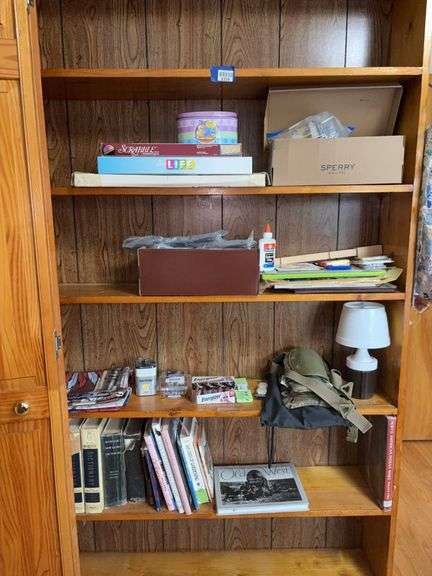 Contents of four shelves: games, greeting cards, office supplies, batteries, battery lamp, books