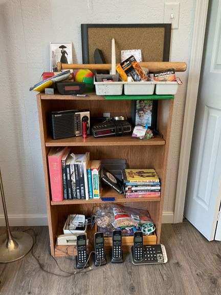 Shelf & contents of shelf unit: digital clock/radio, portable radio, books, DVDs, Panasonic cordless phone system, misc