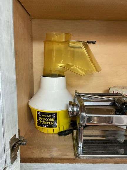 Contents of cupboard: apple peeler, popcorn maker, pasta machine, electric knife in box