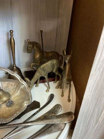 Contents of shelf: metalware - brass figurines and bells, aluminum basket, plated items, flatware