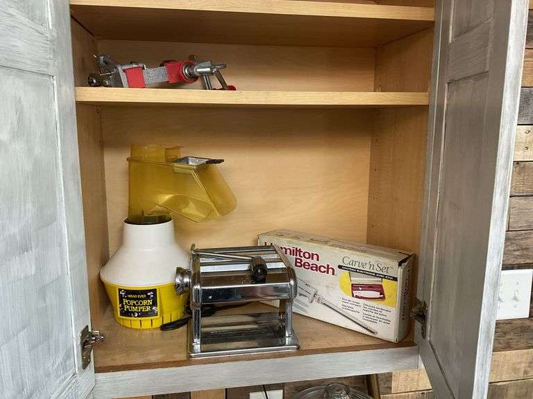 Contents of cupboard: apple peeler, popcorn maker, pasta machine, electric knife in box