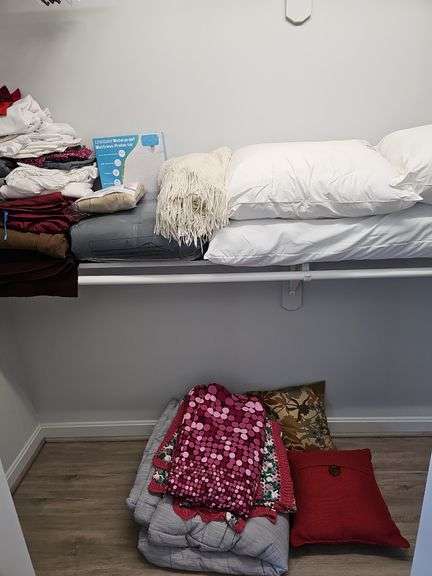 Contents of shelf and on floor below: pillows, sheets, throw, throw pillows, and area rug beside bed