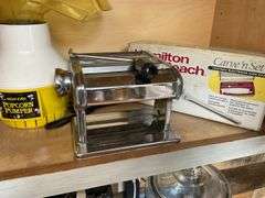 Contents of cupboard: apple peeler, popcorn maker, pasta machine, electric knife in box
