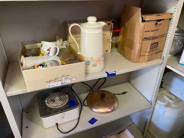 Contents of two shelves: Garfield and Snoopy glasses, beverage pitcher, apple peeler, Rocket Chef food processor, hotplate, misc