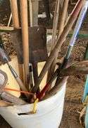 Plastic barrel containing handled tools-shovels, potato fork, rake, pruning shears, pry bar