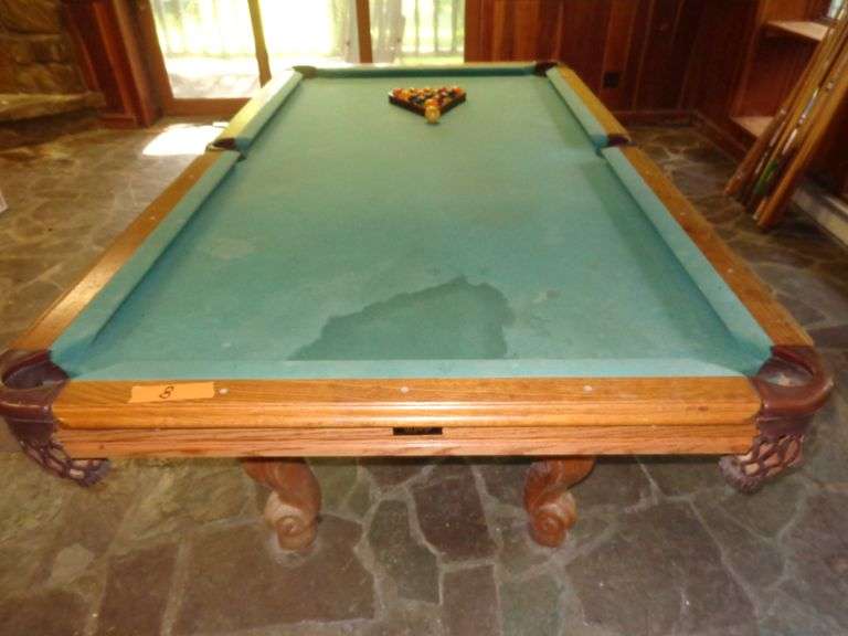 Pool table with billiards balls and 12 pool cues, has stains on felt. Bumper rails may need replaced