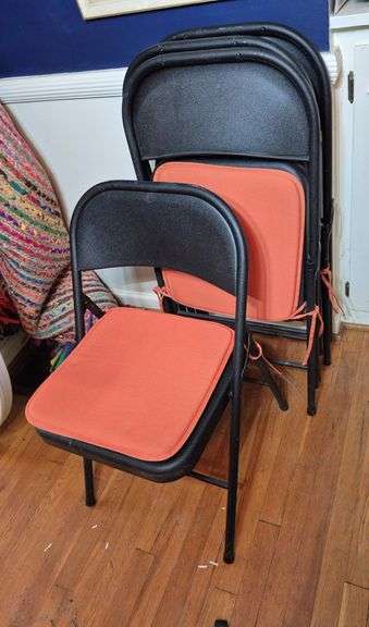 Four metal folding chairs with orange seat cushions
