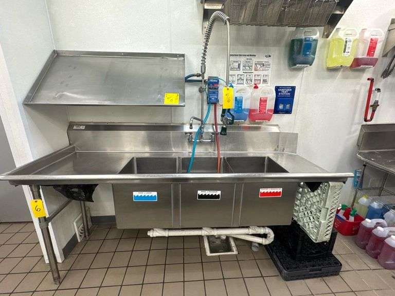 Regency Dishwashing 3-Compartment Stainless Steel Sink 600CDT48RT w/ Drainboards & Pre-Rinse Sprayer w/ Stainless Steel Table, Overhead Bottle Rack Wall Mounted Counter, and Detergent / Sanitizer dispensers.