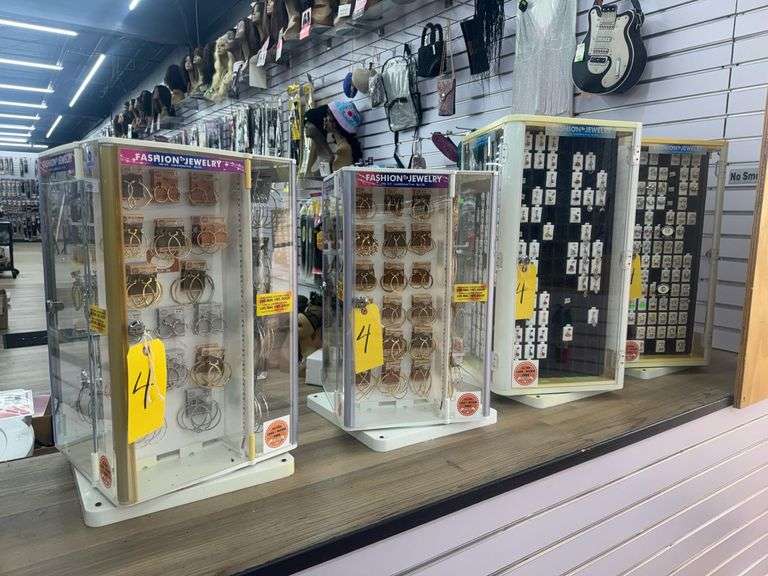 Lot of (4) Tabletop Rotating Display Cases w/ Locking Plexiglass Doors. Includes Fashion Jewelry Including Earrings, Nose Rings, and Face Piercing Jewelry. (2) Cases Measure 12” X 12” X 21”, and (2) Cases Measure 14” X 14” X 27”. These are screwed to shelf, screwdriver or drill required for removal. Single key fits all (4) Cases.