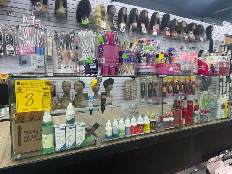 (2) Tabletop Glass Display Shelves 49” X 10” X 11” w/ Contents. Contents Includes Edge Brushes, Bonding Adhesives, Hair Oils. Eyebrow Razors, Stainless Blades, Fashion Rings, Wig Caps, and Hair Weaving Threads