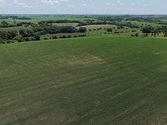 Drone view of 118.86 acres of farmland for sale in Floyd County, Iowa, showcasing expansive row crop fields and rural Iowa landscape under a clear sky.
