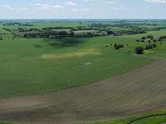 Drone view of 118.86 acres of farmland for sale in Floyd County, Iowa, showcasing expansive row crop fields and rural Iowa landscape under a clear sky.