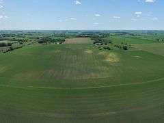 Drone view of 118.86 acres of farmland for sale in Floyd County, Iowa, showcasing expansive row crop fields and rural Iowa landscape under a clear sky.