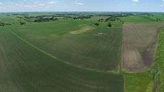 Drone view of 118.86 acres of farmland for sale in Floyd County, Iowa, showing a homestead with outbuildings and expansive row crop fields stretching into the distance.