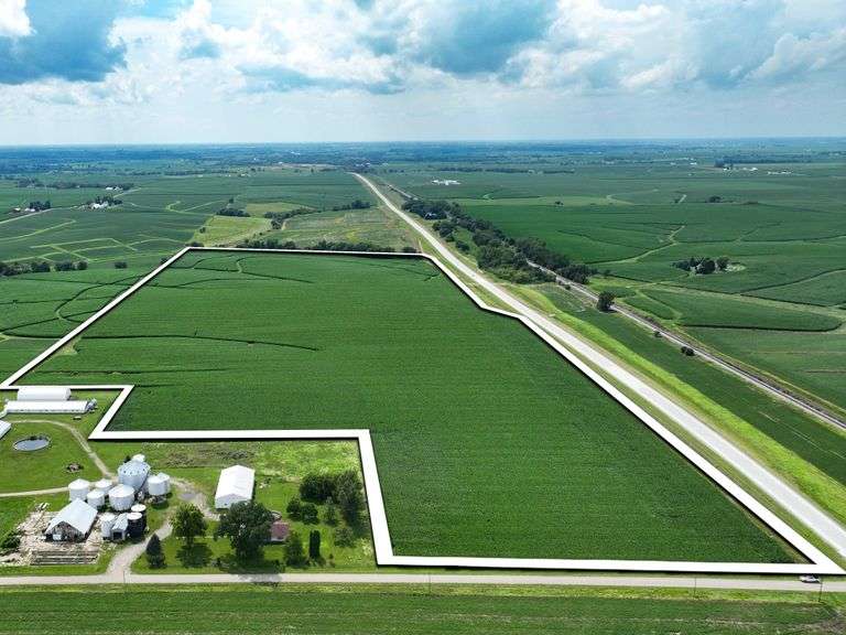 High-elevation drone image of a 77-acre Washington County, Iowa row-crop tract for sale—outlined in white—with contiguous soybean fields and extensive frontage on a paved highway.