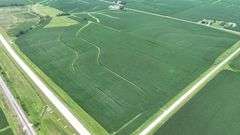 High-angle drone image of a 106-acre Washington County row-crop farm for sale, its irregular boundary outlined in white and bordered by hard-surface roads and rolling green countryside.