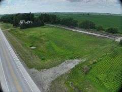 Drone view of a 72-acre Washington County, Iowa tract for sale—open grass frontage between a paved highway and adjacent railroad line, leading into rolling farmland beyond.