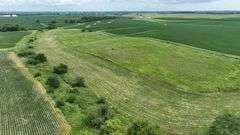 Aerial view of a 30-acre Washington County parcel for sale, featuring a central grassland plateau bordered by lush row-crop fields, scattered trees, and rolling farmland.