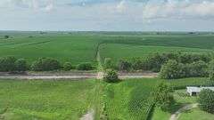 Drone view of a 72-acre Washington County, Iowa tract for sale—open grass frontage between a paved highway and adjacent railroad line, leading into rolling farmland beyond.
