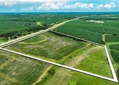 High-angle drone photo of a 27-acre Washington County, Iowa parcel outlined in white, showing contour-planted ground, grass waterways, and paved highway frontage.