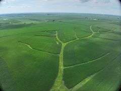 Aerial view of a 70-acre Washington County, Iowa farm for sale—lush cornfields shaped by branching grass waterways, bordered by a paved highway and timbered rail corridor.