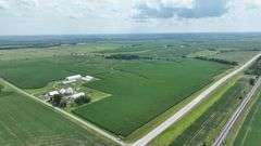 Aerial drone view of a 77-acre Washington County, Iowa row-crop farm for sale—continuous green soybean fields bordered by two paved roads and set amid rolling countryside.