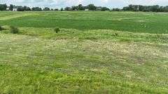 Low-elevation drone view of rolling native grassland dotted with small shrubs and a few trees, part of a 27-acre Washington County, Iowa parcel for sale.