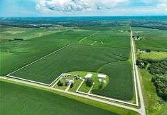 Aerial view of a 42-acre Washington County farm—row-crop fields, two machine sheds, two grain bins, and paved road frontage—outlined for sale.
