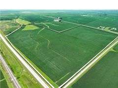 High-angle drone image of a 106-acre Washington County row-crop farm for sale, its irregular boundary outlined in white and bordered by hard-surface roads and rolling green countryside.