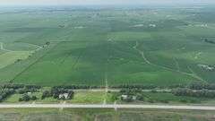 Aerial view of a 72-acre Washington County, Iowa row-crop field for sale—uniform green soybeans on gently rolling ground bordered by grass waterways and a nearby paved highway.