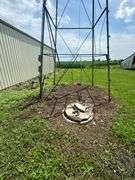 Ground-level view of a steel utility tower frame and capped concrete well beside a metal machine shed on a 42-acre Washington County, Iowa farm for sale.