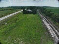 Drone view of a 72-acre Washington County, Iowa tract for sale—open grass frontage between a paved highway and adjacent railroad line, leading into rolling farmland beyond.