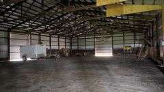 Interior of a spacious machine shed on a 42-acre Washington County, Iowa farm for sale—showing steel siding, open truss roof, concrete floor, and parked farm trailers.