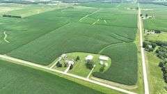 Aerial drone photograph of a 42-acre Washington County farmland tract for sale, showing lush row-crop fields plus two white machine sheds and two round grain bins along a paved road.