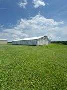 Drone view of a weathered open-front machine shed and two silver grain bins set amid lush cornfields—part of a 42-acre Washington County, Iowa farm for sale.